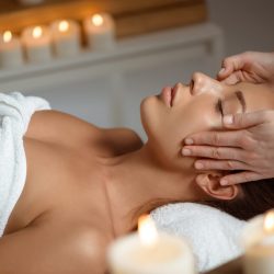 Young beautiful brunette girl having face massage relaxing in spa salon. Eyes closed. Copy space.